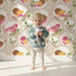 Lovely child standing in front of Whimsy Tots Garden Songbird Parade Wallpaper in Beige with bird, branch, leaf, berry in design.