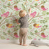Lovely child standing in front of Whimsy Tots Blossom Branch Birds Wallpaper in Mint Green with bird, berry, leaf, branch in design.