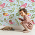 Lovely child standing in front of Whimsy Tots Blossom Branch Birds Wallpaper in Sky Blue with bird, branch, leaf, berry in design.
