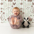 Lovely child standing in front of Whimsy Tots Meadow Hop Bunnies Wallpaper in Sage Green with rabbit, flower, bunny, leaf, stripe in design.