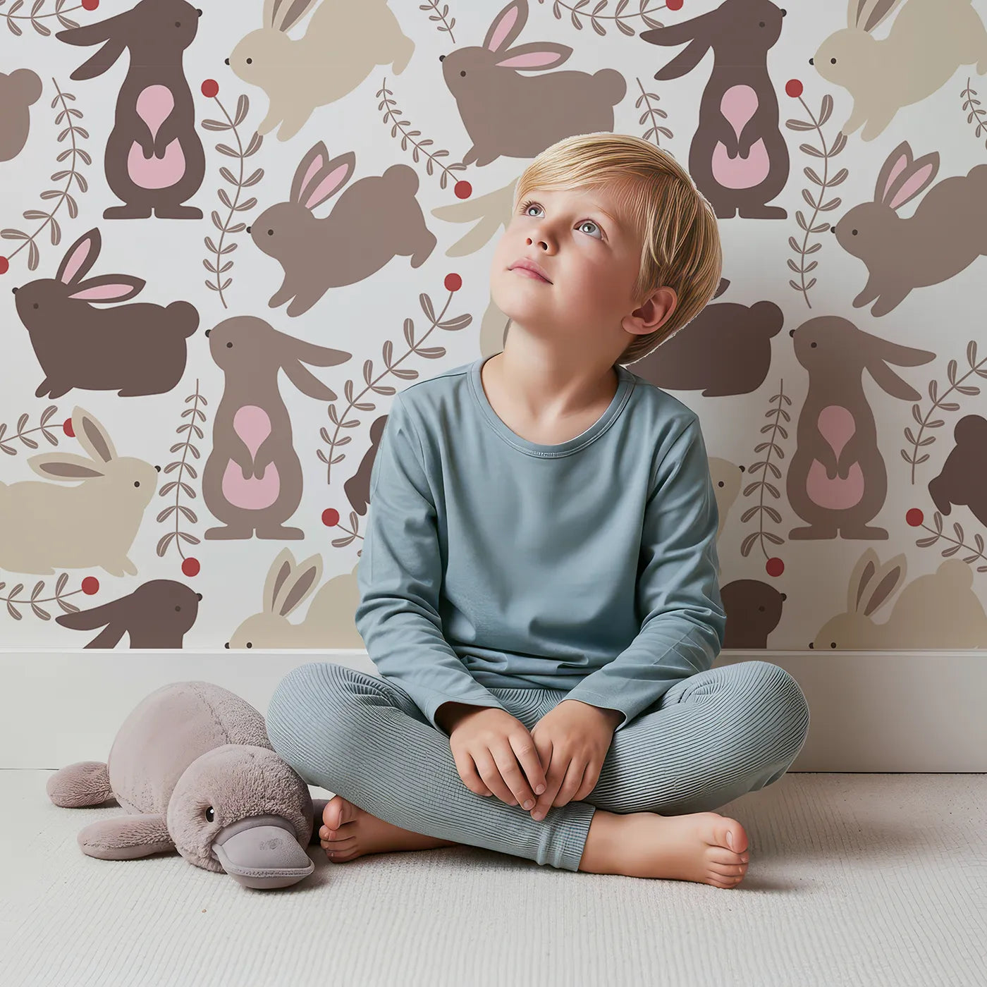 Lovely child standing in front of Whimsy Tots Berry Bunny Parade Wallpaper in Cocoa with rabbit, bunny, leaf, berry, sprig in design.