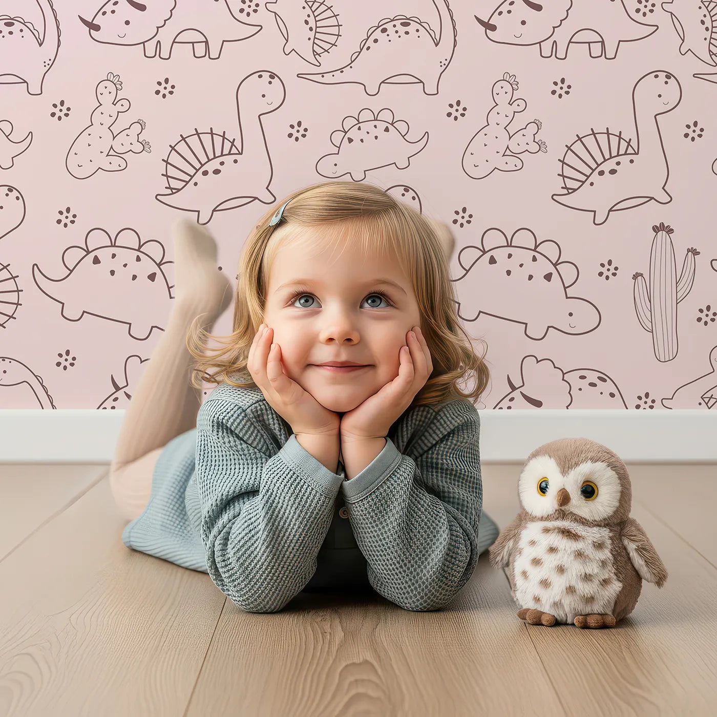 Lovely child standing in front of Whimsy Tots Desert Dino Parade Wallpaper in Blush Pink with dinosaur, cactus, flower in design.
