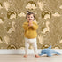 Lovely child standing in front of Whimsy Tots Dino Circle Parade Wallpaper in Earth Tones with dinosaur, flower, heart, circle in design.