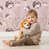 Lovely child standing in front of Whimsy Tots Dino Circle Parade Wallpaper in Blush Pink with dinosaur, flower, heart, circle in design.