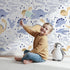 Lovely child standing in front of Whimsy Tots Cactus Canyon Dinos Wallpaper in White with dinosaur, cactus, rock, spike in design.
