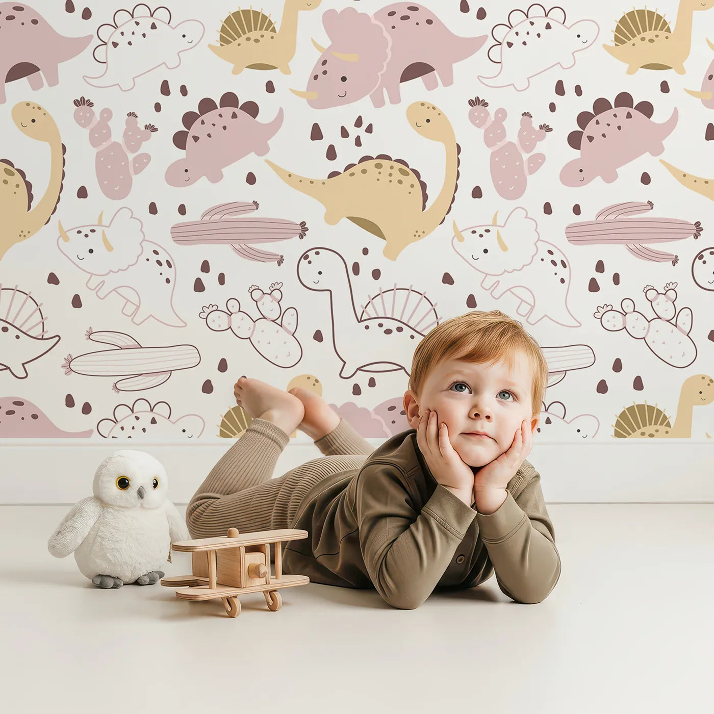 Lovely child standing in front of Whimsy Tots Cactus Canyon Dinos Wallpaper in Blush Pink with dinosaur, cactus, rock, spike in design.