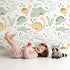 Lovely child standing in front of Whimsy Tots Cactus Canyon Dinos Wallpaper in Mint Green with dinosaur, cactus, rock, spike in design.