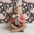 Lovely child standing in front of Whimsy Tots Starlit Swan Ballet Wallpaper in Charcoal Black with swan, crown, flower, bow, leaf in design.