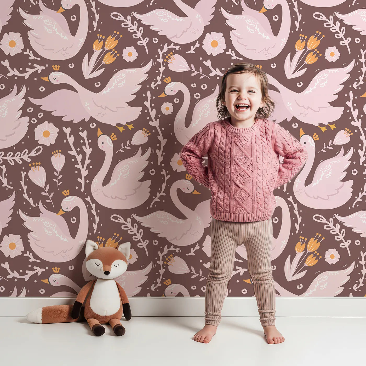 Lovely child standing in front of Whimsy Tots Starlit Swan Ballet Wallpaper in Cocoa Brown with swan, crown, flower, bow, leaf in design.
