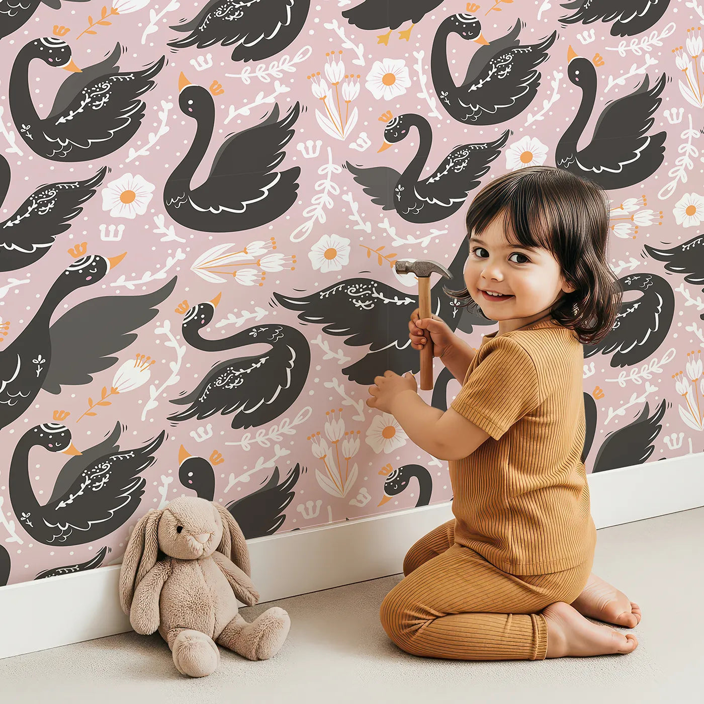 Lovely child standing in front of Whimsy Tots Regal Swan Parade Wallpaper in Blush Pink with swan, flower, crown, leaf in design.