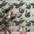 Lovely child standing in front of Whimsy Tots Regal Swan Parade Wallpaper in Sage Green with swan, flower, crown, leaf in design.