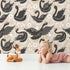 Lovely child standing in front of Whimsy Tots Regal Swan Parade Wallpaper in Beige with swan, flower, crown, leaf in design.