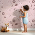 Lovely child standing in front of Whimsy Tots Floral Fox Cuddles Wallpaper in Blush Pink with fox, flower, leaf in design.