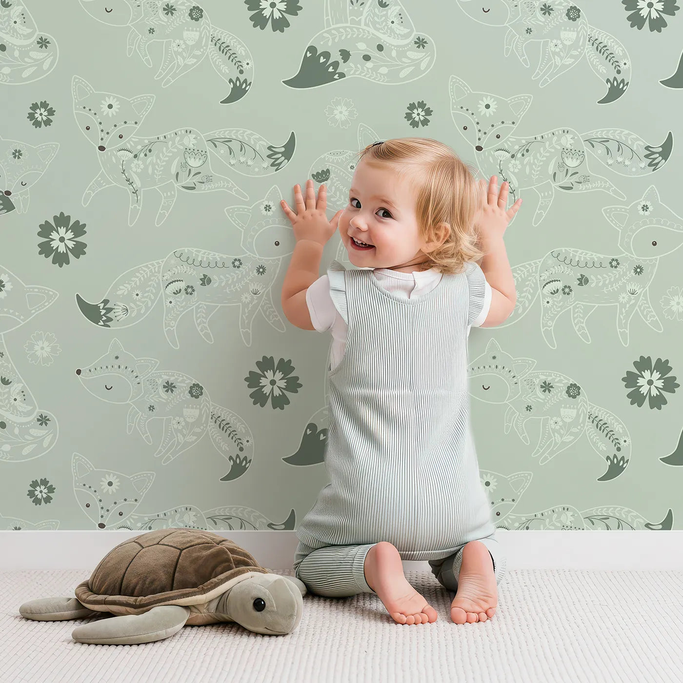 Lovely child standing in front of Whimsy Tots Floral Fox Cuddles Wallpaper in Sage Green with fox, flower, leaf in design.