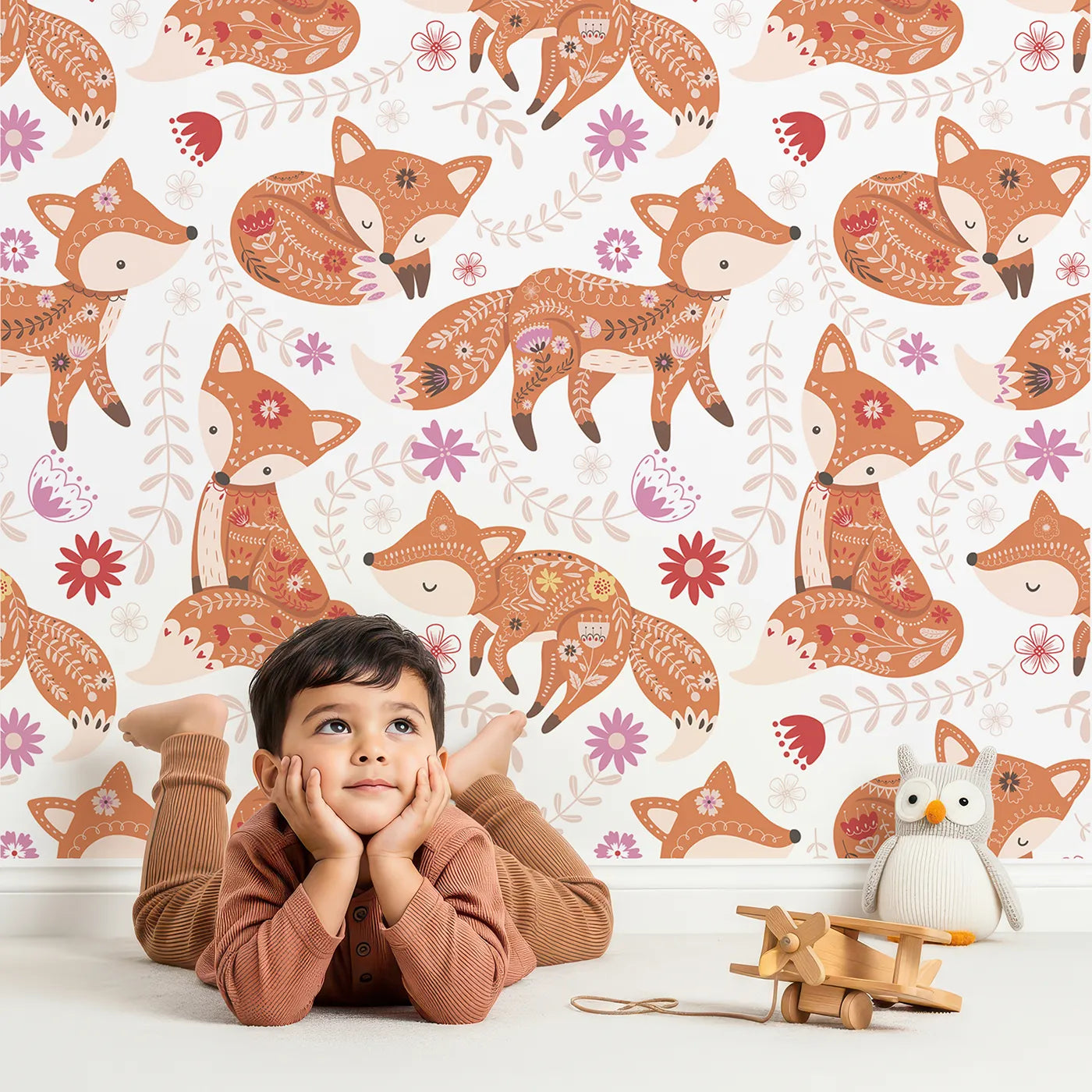 Lovely child standing in front of Whimsy Tots Folk Tale Foxes Wallpaper in Autumn Spice with fox, flower, leaf in design.