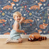 Lovely child standing in front of Whimsy Tots Folk Bloom Foxes Wallpaper in Twilight Blue with fox, flower, vine in design.