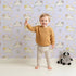 Lovely child standing in front of Whimsy Tots Cozy Pawstep Kittens Wallpaper in Lavender Purple with cat, kitten, pawprint, spot in design.