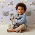 Lovely child standing in front of Whimsy Tots Whisker Wink Kitty Wallpaper in Lavender Purple with cat, pawprint, whisker, smile in design.