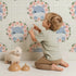 Lovely child standing in front of Whimsy Tots Blossom Hippo Winks Wallpaper in Mint Plaid Green with hippo, flower, wreath, plaid in design.