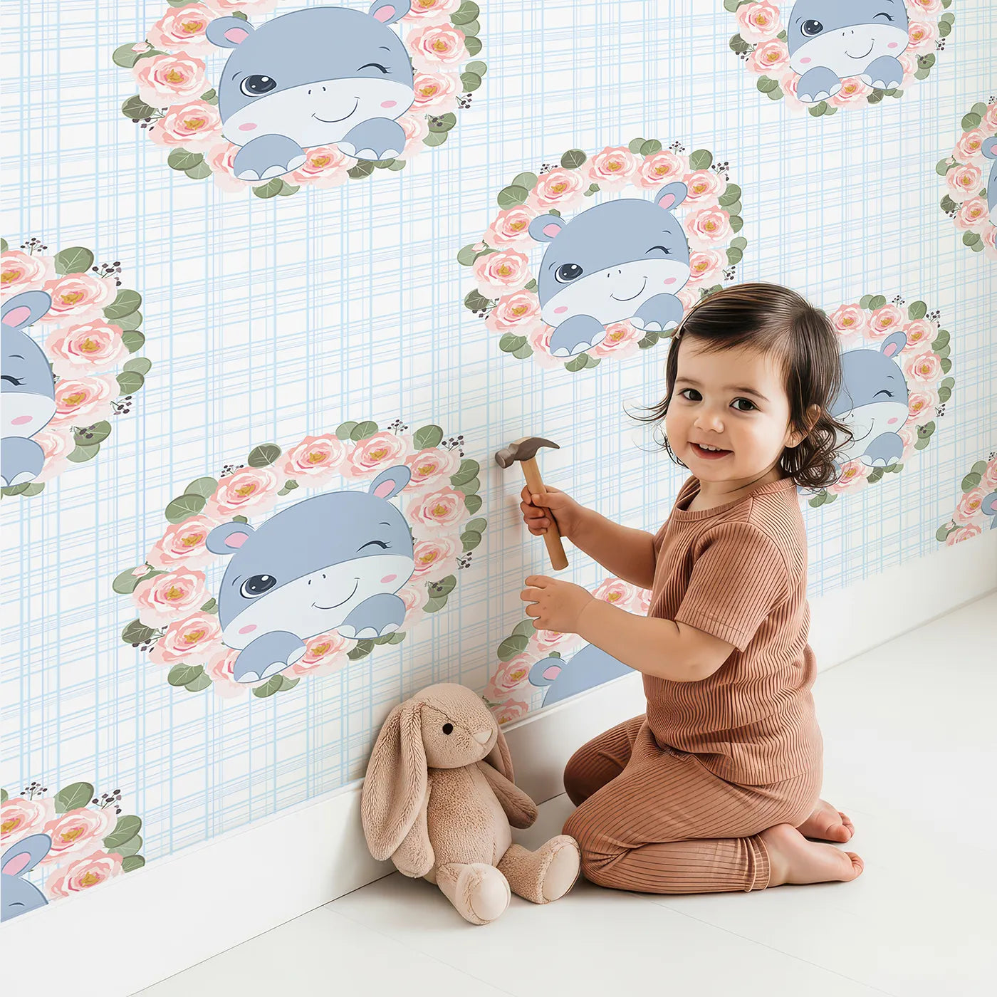 Lovely child standing in front of Whimsy Tots Blossom Hippo Winks Wallpaper in Sky Plaid with hippo, flower, wreath, rose in design.