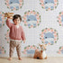 Lovely child standing in front of Whimsy Tots Blossom Hippo Winks Wallpaper in Lavender Plaid with hippo, flower, wreath, plaid in design.