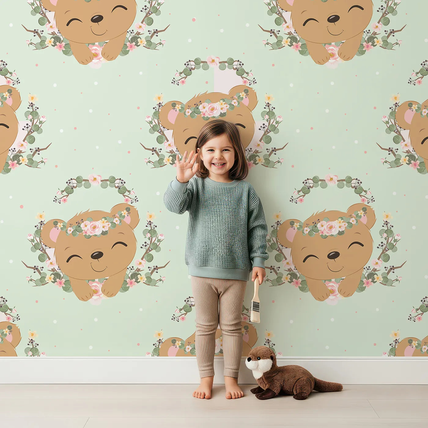 Lovely child standing in front of Whimsy Tots Floral Bear Hugs Wallpaper in Mint Green with bear, flower, crown, branch, leaf in design.