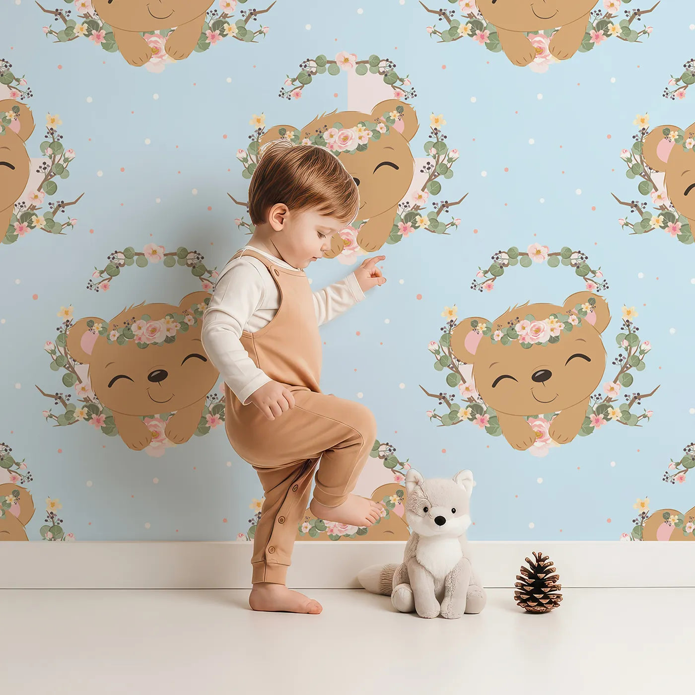 Lovely child standing in front of Whimsy Tots Floral Bear Hugs Wallpaper in Sky Blue with bear, flower, crown, branch, leaf in design.