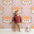 Lovely child standing in front of Whimsy Tots Floral Fox Peek Wallpaper in Rosewood Blush Pink with fox, flower, crown, leaf, polka in design.