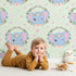 Lovely child standing in front of Whimsy Tots Floral Elephant Wink Wallpaper in Minty Meadow Green with elephant, heart, flower, crown, branch, leaf in design.