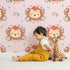Lovely child standing in front of Whimsy Tots Little Lion Blossom Parade Wallpaper in Blush Petal Pink with lion, flower, wreath, leaf, blossom in design.