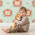 Lovely child standing in front of Whimsy Tots Little Lion Blossom Parade Wallpaper in Mint Whimsy Green with lion, flower, wreath, leaf, blossom in design.