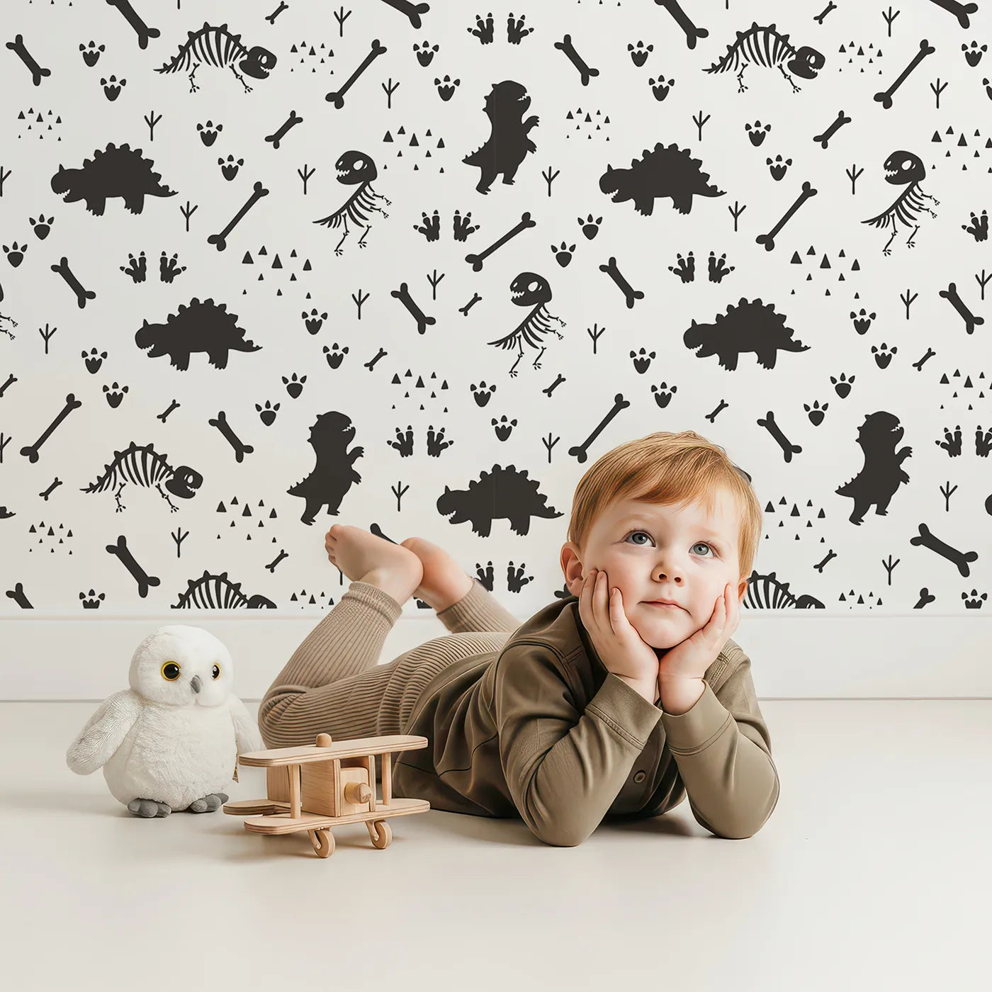 Lovely child standing in front of Whimsy Tots Dino Fossil Footprints Wallpaper in Black & White with dinosaur, fossil, bone, footprint in design.