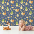 Lovely child standing in front of Whimsy Tots Hatchling Dino Parade Wallpaper in Dusty Denim with dinosaur, egg, bone, flower in design.