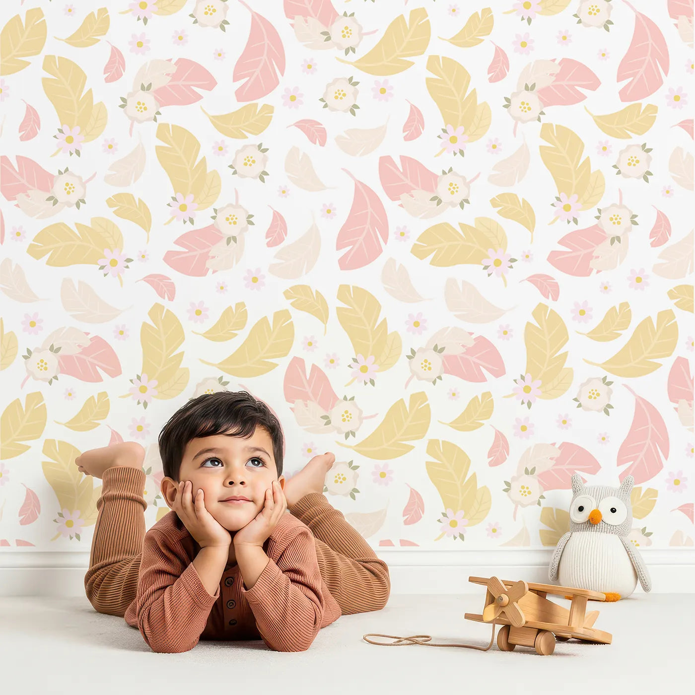 Lovely child standing in front of Whimsy Tots Floral Feather Drift Wallpaper in Petal White with feather, flower, blossom, leaf in design.