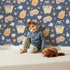 Lovely child standing in front of Whimsy Tots Blossom Basket Friends Wallpaper in Twilight Blue with fox, mouse, flower, basket, crown in design.