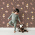 Lovely child standing in front of Whimsy Tots Blush Ballerina Dreams Wallpaper Pink with ballerina, crown, tutu, slipper, flower in design.