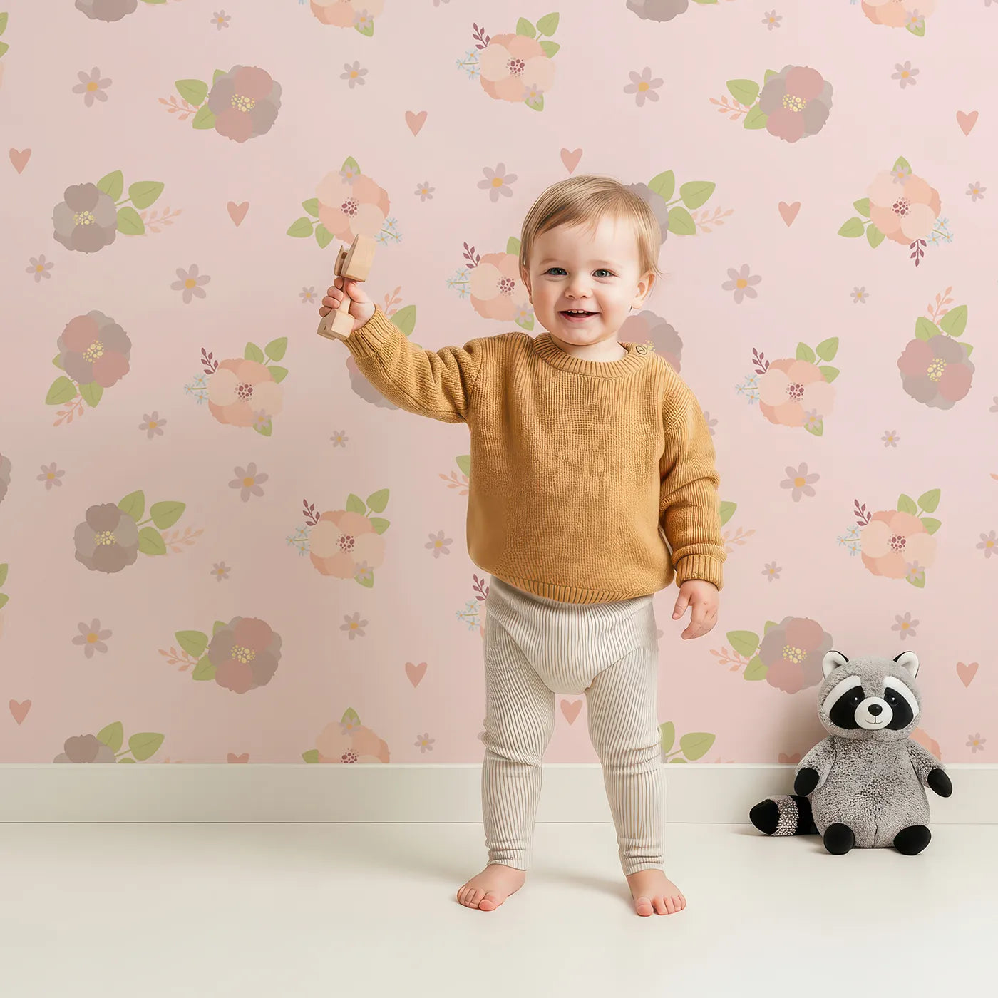 Lovely child standing in front of Whimsy Tots Soft Garden Posy Wallpaper in Petal Pink with flower, bouquet, leaf, heart in design.