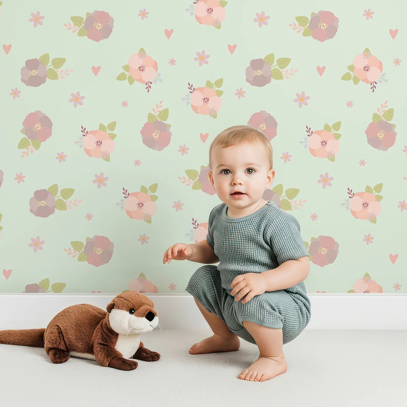 Lovely child standing in front of Whimsy Tots Soft Garden Posy Wallpaper in Mint Meadow Green with flower, bouquet, leaf, heart in design.