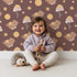 Lovely child standing in front of Whimsy Tots Moonlit Bear Dreams Wallpaper in Cocoa Night Brown with bear, flower, moon, star in design.