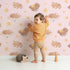 Lovely child standing in front of Whimsy Tots Woodland Nap Parade Wallpaper in Soft Mint Green with bear, bunny, fox, flower, star in design.