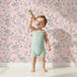 Lovely child standing in front of Whimsy Tots Wildflower Scribble Garden Wallpaper in Blush Sketch Pink with flower, leaf, berry, sketch, doodle in design.