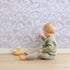 Lovely child standing in front of Whimsy Tots Doodle Meadow Shapes Wallpaper in Lavender with doodle, shape, scribble, petal, arch in design.
