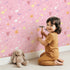 Lovely child standing in front of Whimsy Tots Cupids Arrow Parade Wallpaper in Blush Pink with arrow, heart, star in design.