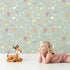 Lovely child standing in front of Whimsy Tots Cupids Arrow Parade Wallpaper in Sage Whimsy Green with arrow, heart, star in design.