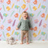 Lovely child standing in front of Whimsy Tots Feathered Joy Parade Wallpaper in Lavender Lilac with bird, feather, sprig, arrow in design.