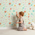 Lovely child standing in front of Whimsy Tots Love and Arrows Bloom Parade Wallpaper in Mint Green with arrow, heart, flower, burst in design.