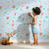 Lovely child standing in front of Whimsy Tots Love and Arrows Bloom Parade Wallpaper in Sky Blue with arrow, heart, flower, burst in design.