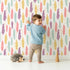 Lovely child standing in front of Whimsy Tots Feather and Arrow Meadow Parade Wallpaper in Cream White with feather, arrow, leaf in design.