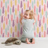 Lovely child standing in front of Whimsy Tots Feather and Arrow Meadow Parade Wallpaper in Blush Pink with feather, arrow, leaf in design.