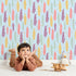 Lovely child standing in front of Whimsy Tots Feather and Arrow Meadow Parade Wallpaper in Sky Blue with feather, arrow, leaf in design.